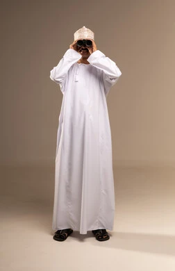 توضيح الرؤية عبر التلسكوب, حب الاستكشاف و المغامرة, بورتريه لرجل عربي خليجي عماني يرتدي الدشداشة والكمه يحمل بيده منظار ثنائي العينين و ينظر الى شيء ما, تقريب الأشياء والأماكن البعيدة، إيماءات الاستمتاع والسرور, صورة الجسم بالطول الكامل, خلفية بيج