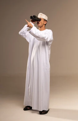 Bringing distant objects and places closer, gestures of enjoyment and pleasure, love for exploration and adventure, clarifying vision through a telescope, a portrait of an Arab Gulf Omani man wearing a dishdasha and kumma holding a binocular in his hand and looking at something, full-body image, beige background.