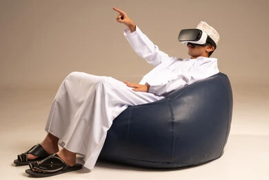 Integration and interaction with the imaginary world, using advanced technologies and technology, a portrait of a young Arab Gulf Omani man wearing a dishdasha and an Omani kumma, wearing AR glasses on his eyes, watching virtual reality movies, spending leisure time in an enjoyable way, beige background.