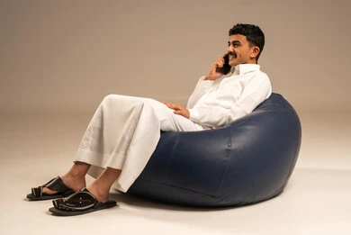 Making a phone call, using modern devices and technologies, a portrait of an Arab Gulf Saudi man wearing traditional attire sitting on a chair in a comfortable position holding a mobile phone in his hand with gestures of joy, communicating with family and friends, browsing social media, gray background.