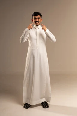 العناية والتجميل والتبيض، تعابير السرور باستخدام قشور فينير من الخزف، بورتريه لشاب عربي خليجي سعودي مبتسم يرتدي الزي التقليدي ينظر إلى الكاميرا يشير بيديه إلى أسنانه, أهمية متابعة طبيب الاسنان، خلفية رمادية