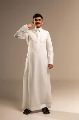 العناية والتجميل والتبيض، بورتريه لرجل عربي خليجي سعودي يرتدي الثوب التقليدي يشير إلى أسنانه بإيماءات السرور، النظر الى الكاميرا بتعابير السعادة، استخدام قشور فينير من الخزف لصنع ابتسامة ناصعه، أهمية متابعة طبيب الاسنان، الطول الكامل للجسم، خلفية بيضاء