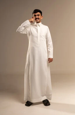 العناية والتجميل والتبيض، بورتريه لرجل عربي خليجي سعودي يرتدي الزي التقليدي يشير إلى أسنانه بإيماءات السرور، النظر الى الكاميرا بتعابير السعادة، استخدام قشور فينير من الخزف لصنع ابتسامة ناصعه، أهمية متابعة طبيب الاسنان، الطول الكامل للجسم، خلفية بيضاء