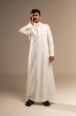 التركيز على الكلام و محاولة سماع الأصوات، الانصات وحسن الاستماع, حدوث ضعف في السمع, بورتريه لرجل عربي خليجي سعودي يرتدي الثوب التقليدي يضع يده خلف اذنه بإيماءات التنصت, الجسم بالطول الكامل, خلفية رمادية