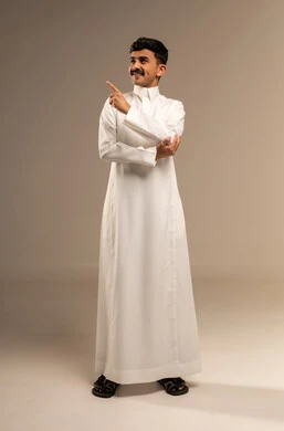 Indicating and clarifying something, specifying a certain location, pointing to the place of an element, a portrait of a young Arab Gulf Saudi man wearing traditional attire pointing with his index finger to something, full-body image, gray background.