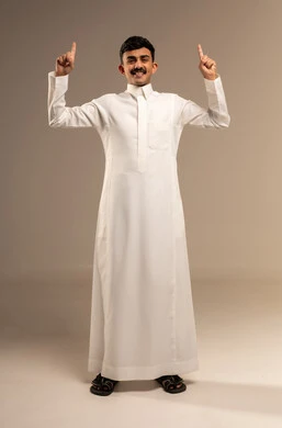 تحديد موقع معين, النظر إلى الكاميرا بإيماءات السرور، الإشارة و التوضيح إلى شيء ما, الدلالة على مكان عنصر، بورتريه لشاب عربي خليجي سعودي يرتدي الثوب التقليدي يشير بإصبع السبابة إلى الاعلى, صورة الجسم بالطول الكامل، خلفية رمادية