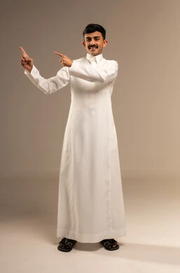الإشارة و التوضيح إلى شيء ما, تحديد موقع معين, الدلالة على مكان عنصر، بورتريه لشاب عربي خليجي سعودي يرتدي الثوب التقليدي يشير بإصبع السبابة إلى شيء ما, صورة الجسم بالطول الكامل، خلفية رمادية