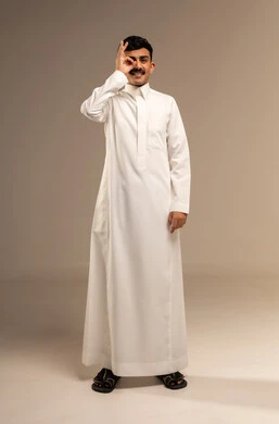 The concept of planning and future vision, a portrait of a smiling young Arab Gulf Saudi man wearing traditional attire, placing his hand over his eyes in a circular lens shape with gestures of searching and exploration, full-body, gray background.