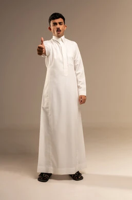 Gestures indicating agreement and acceptance, a portrait of a young Arab Gulf Saudi man wearing traditional attire, pointing his thumb up, showing expressions of joy and happiness, satisfaction, and non-rejection, with a gray background.