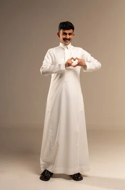 اظهار مشاعر الحب والشغف، مفهوم المحبة والمودة، بورتريه لشاب عربي خليجي سعودي يرتدي الزي التقليدي يرفع يديه بإيماءات على شكل قلب، تعابير الفرح والسرور والسعادة، صورة الجسم بالطول الكامل, خلفية رمادية