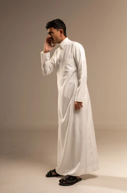 Shouting and speaking in a loud tone to be heard well, calling out in a loud voice, placing the hand next to the mouth to amplify the sounds, a portrait of a young Arab Gulf Saudi man looking at the camera with gestures calling someone, conversations and social communication, full-body, gray background.