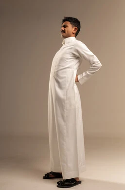 الحاجه للراحه من التعب والإرهاق , الاحساس بألم في العمود الفقري , بورتريه لشاب عربي خليجي سعودي يرتدي  الزي التقليدي يضع يده اسفل ظهره بتعابير الشعور بالوجع, طلب المساعده للذهاب الى الطبيب ,صورة الجسم بالكامل، خلفية رمادية