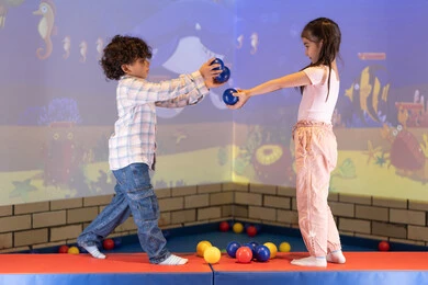 Enjoying playing in an amusement park, an entertainment center, an Emirati Gulf Arab girl having a fun time playing an interactive throwing game with her brother, expressions of joy and happiness, moments of fun and excitement, spending happy times, a joyful interactive atmosphere.