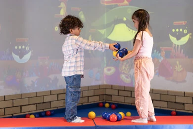 Entertainment center, expressions of joy and happiness, moments of fun and excitement, spending happy times in an amusement park, a cheerful interactive atmosphere, an Emirati Gulf Arab girl enjoying a fun time playing an interactive throwing game with her brother.