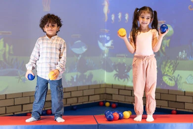 تعابير السرور والسعادة، لحظات المرح والحماس، قضاء الاوقات السعيده فى مدينه الالعاب ،أجواء تفاعلية مبهجة ،بنت عربية خليجية إماراتية تستمتع بوقت ممتع في لعبة الرمي التفاعلية برفقه اخوها ،مركز ألعاب ترفيهي