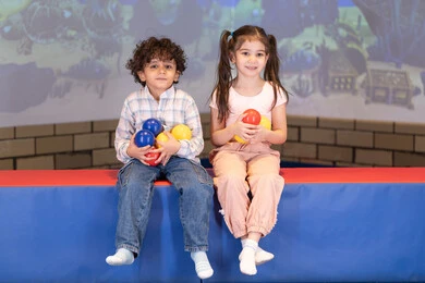Spending happy times at an amusement park, a joyful interactive atmosphere, an Emirati Gulf Arab girl enjoying an interactive throwing game with her brother, an amusement center, expressions of joy and happiness, moments of fun and excitement.