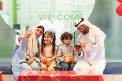 استخدام الجوال لتوثيق اللحظات التذكاريه ،عائلة عربية خليجية إماراتية تستمتع بوقت ممتع في لعبة الرمي التفاعلية، رجل اماراتي  يلتقط صور السيلفي ،أجواء تفاعلية مبهجة ، قضاء الاوقات السعيده مع الابناء ، مركز ألعاب ترفيهي، تعابير السرور والسعادة،  مشاركة الأب والأم أطفالهما لحظات المرح والحماس