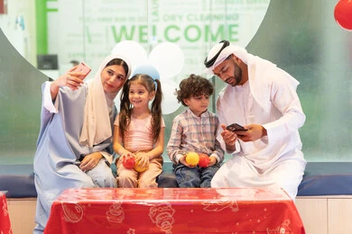 عائلة عربية خليجية إماراتية تستمتع بوقت ممتع في لعبة الرمي التفاعلية، رجل اماراتي  يلتقط صور السيلفي ،أجواء تفاعلية مبهجة ، قضاء الاوقات السعيده مع الابناء ، مركز ألعاب ترفيهي،استخدام الجوال لتوثيق اللحظات التذكاريه ، تعابير السرور والسعادة،  مشاركة الأب والأم أطفالهما لحظات المرح والحماس