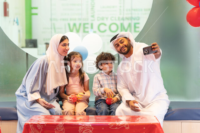 رجل اماراتي  يلتقط صور السيلفي ،أجواء تفاعلية مبهجة ، قضاء الاوقات السعيده مع الابناء ، مركز ألعاب ترفيهي،استخدام الجوال لتوثيق اللحظات التذكاريه ، تعابير السرور والسعادة،  مشاركة الأب والأم أطفالهما لحظات المرح والحماس ،عائلة عربية خليجية إماراتية تستمتع بوقت ممتع في لعبة الرمي التفاعلية