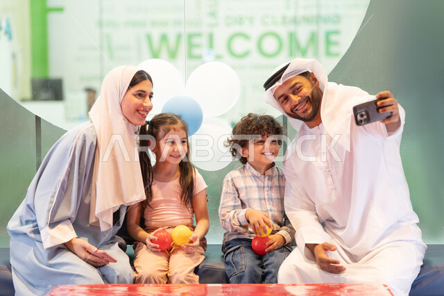 أجواء تفاعلية مبهجة ، قضاء الاوقات السعيده مع الابناء ، مركز ألعاب ترفيهي،استخدام الجوال لتوثيق اللحظات التذكاريه ، تعابير السرور والسعادة،  رجل اماراتي  يلتقط صور السيلفي ،مشاركة الأب والأم أطفالهما لحظات المرح والحماس ،عائلة عربية خليجية إماراتية تستمتع بوقت ممتع في لعبة الرمي التفاعلية