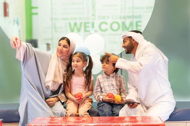 تعابير السرور والسعادة، سيده اماراتيه تلتقط صور السيلفي ،مشاركة الأب والأم أطفالهما لحظات المرح والحماس ، مركز ألعاب ترفيهي،استخدام الجوال لتوثيق اللحظات التذكاريه ، أجواء تفاعلية مبهجة ، عائلة عربية خليجية إماراتية تستمتع بوقت ممتع في لعبة الرمي التفاعلية ، قضاء الاوقات السعيده مع الابناء
