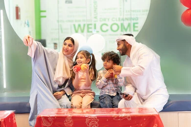 سيده اماراتيه تلتقط صور السيلفي ،مشاركة الأب والأم أطفالهما لحظات المرح والحماس ، مركز ألعاب ترفيهي،استخدام الجوال لتوثيق اللحظات التذكاريه ، أجواء تفاعلية مبهجة ، عائلة عربية خليجية إماراتية تستمتع بوقت ممتع في لعبة الرمي التفاعلية ،تعابير السرور والسعادة،  قضاء الاوقات السعيده مع الابناء