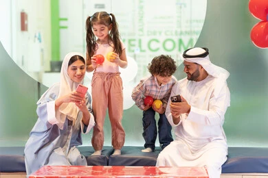 Taking selfies, an entertainment game center, using mobile phones to document memorable moments, parents sharing moments of fun and excitement with their children, a cheerful interactive atmosphere, an Arab Gulf Emirati family enjoying a fun time in the interactive throwing game, expressions of pleasure and happiness, spending happy times with the children