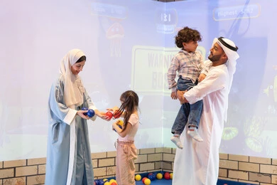 مركز ألعاب ترفيهي، مشاركة الأب والأم أطفالهما لحظات المرح والحماس ،  أجواء تفاعلية مبهجة ، اب اماراتي يحمل ابنه لاعلى بتعابير البهجه ، عائلة عربية خليجية إماراتية تستمتع بوقت ممتع في لعبة الرمي التفاعلية ،تعابير السرور والسعادة،  قضاء الاوقات السعيده مع الابناء