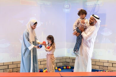 أجواء تفاعلية مبهجة ، اب اماراتي يحمل ابنه لاعلى بتعابير البهجه ، عائلة عربية خليجية إماراتية تستمتع بوقت ممتع في لعبة الرمي التفاعلية ،تعابير السرور والسعادة،  قضاء الاوقات السعيده مع الابناء ،مركز ألعاب ترفيهي، مشاركة الأب والأم أطفالهما لحظات المرح والحماس