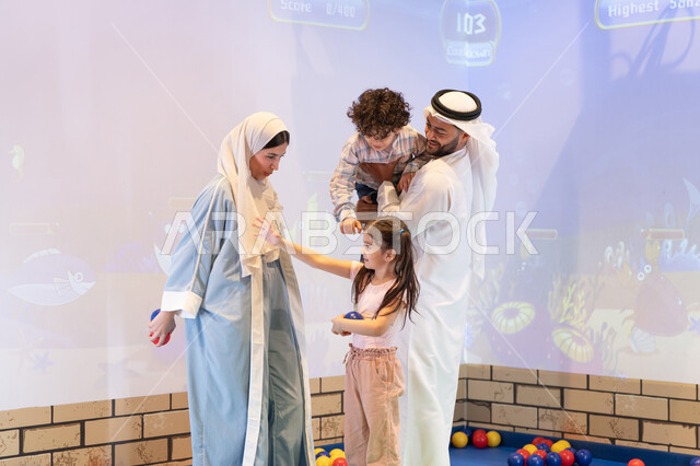 عائلة عربية خليجية إماراتية تستمتع بوقت ممتع في لعبة الرمي التفاعلية ،تعابير السرور والسعادة،  قضاء الاوقات السعيده مع الابناء ،مركز ألعاب ترفيهي، مشاركة الأب والأم أطفالهما لحظات المرح والحماس ، أجواء تفاعلية مبهجة