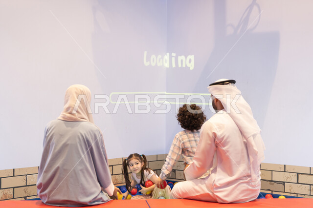مشاركة الأب والأم أطفالهما لحظات المرح والحماس ، أجواء تفاعلية مبهجة ،تعابير السرور والسعادة، مركز ألعاب ترفيهي، صوره من الخلف لعائلة عربية خليجية إماراتية تستمتع بوقت ممتع في لعبة الرمي التفاعلية ، قضاء الاوقات السعيده مع الابناء