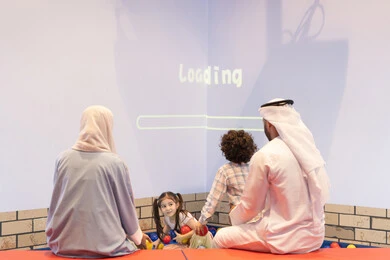 مشاركة الأب والأم أطفالهما لحظات المرح والحماس ، أجواء تفاعلية مبهجة ،تعابير السرور والسعادة، مركز ألعاب ترفيهي، صوره من الخلف لعائلة عربية خليجية إماراتية تستمتع بوقت ممتع في لعبة الرمي التفاعلية ، قضاء الاوقات السعيده مع الابناء