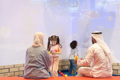 مشاركة الأب والأم أطفالهما لحظات المرح والحماس ،  مركز ألعاب ترفيهي، صوره من الخلف لعائلة عربية خليجية إماراتية تستمتع بوقت ممتع في لعبة الرمي التفاعلية ، أجواء تفاعلية مبهجة ،قضاء الاوقات السعيده مع الابناء ،تعابير السرور والسعادة