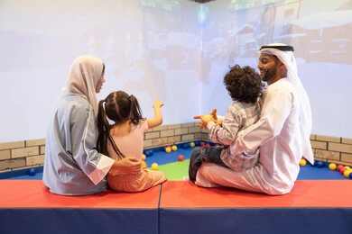 مركز ألعاب ترفيهي، صوره من الخلف لعائلة عربية خليجية إماراتية تستمتع بوقت ممتع في لعبة الرمي التفاعلية ، أجواء تفاعلية مبهجة ،قضاء الاوقات السعيده مع الابناء ،مشاركة الأب والأم أطفالهما لحظات المرح والحماس ، تعابير السرور والسعادة