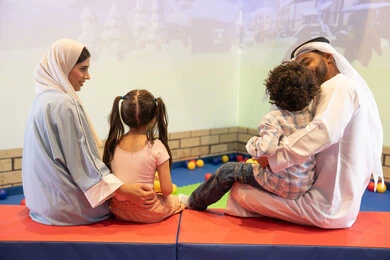 أجواء تفاعلية مبهجة ،قضاء الاوقات السعيده مع الابناء ، صوره من الخلف لعائلة عربية خليجية إماراتية تستمتع بوقت ممتع في لعبة الرمي التفاعلية ، مركز ألعاب ترفيهي، مشاركة الأب والأم أطفالهما لحظات المرح والحماس ، تعابير السرور والسعادة