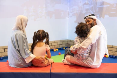 قضاء الاوقات السعيده مع الابناء ، أجواء تفاعلية مبهجة ،صوره من الخلف لعائلة عربية خليجية إماراتية تستمتع بوقت ممتع في لعبة الرمي التفاعلية ، مركز ألعاب ترفيهي، مشاركة الأب والأم أطفالهما لحظات المرح والحماس ، تعابير السرور والسعادة