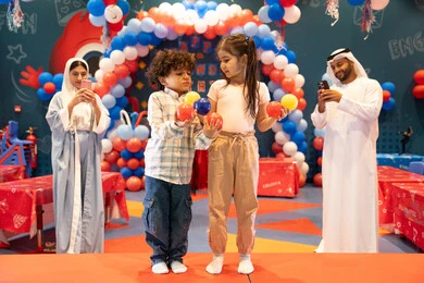 The concept of entertainment and recreation, gestures of pleasure and joy, an Arab Gulf Emirati family enjoying playing in an amusement park, playing with colored balls, integrating advanced technologies into daily life, entertaining entertainment centers in the UAE, using mobile phones to document memorable moments, spending happy times in a funfair.