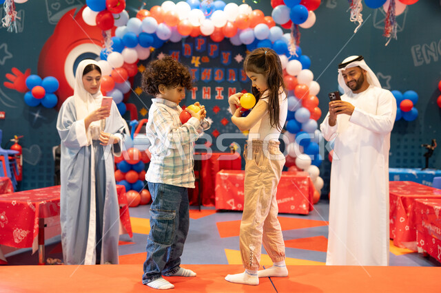 Using mobile phones to document memorable moments, the concept of entertainment and recreation, integrating advanced technologies into daily life, feelings of joy and happiness, spending happy times in a funfair, entertaining entertainment centers in the UAE, an Arab Gulf Emirati family enjoying playing in an amusement park, playing with colored balls.