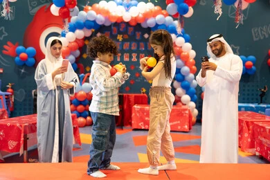Using mobile phones to document memorable moments, the concept of entertainment and recreation, integrating advanced technologies into daily life, feelings of joy and happiness, spending happy times in a funfair, entertaining entertainment centers in the UAE, an Arab Gulf Emirati family enjoying playing in an amusement park, playing with colored balls.