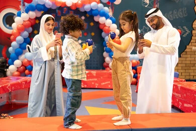 مفهوم التسلية والترفيه، دمج التقنيات المتطوره فى الحياه اليوميه، مشاعر المتعة والفرح، قضاء أوقات سعيده في أرض المرح، المراكز الترفيهيه المسلية في الامارات العربية،عائله عربيه خليجيه اماراتيه تستمتع باللعب فى مدينة الملاهي ، تلعب بالكور الملونه ، استخدام الجوال فى توثيق اللحظات التذكاريه