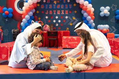 Taking selfies, integrating advanced technologies into daily life, feelings of joy and happiness, spending happy times in the land of fun, entertaining entertainment centers in the UAE, an Arab Gulf Emirati family enjoying playing in an amusement park, playing with colored balls and using a mobile phone, the concept of entertainment and recreation.