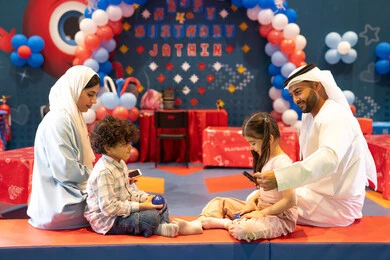 Integrating advanced technologies into daily life, feelings of joy and happiness, spending happy times in the land of fun, entertaining entertainment centers in the UAE, an Arab Gulf Emirati family enjoying playing in an amusement park, playing with colored balls and using a mobile phone, the concept of entertainment and recreation.