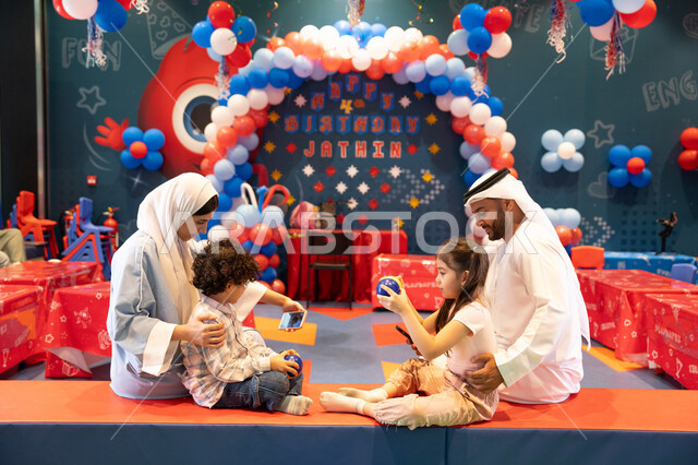 Spending happy times at Funland, the fun entertainment centers in the UAE, an Arab Gulf Emirati family enjoying playing in an amusement park and using a mobile phone, feelings of joy and happiness, the concept of entertainment and recreation, integrating advanced technologies into daily life.