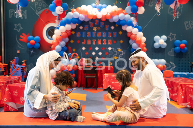 المراكز الترفيهيه المسلية في الامارات العربية، قضاء أوقات سعيده في أرض المرح،عائله عربيه خليجيه اماراتيه تستمتع باللعب فى مدينة الملاهي وتستخدم الجوال ، مشاعر المتعة والفرح، مفهوم التسلية والترفيه، دمج التقنيات المتطوره فى الحياه اليوميه
