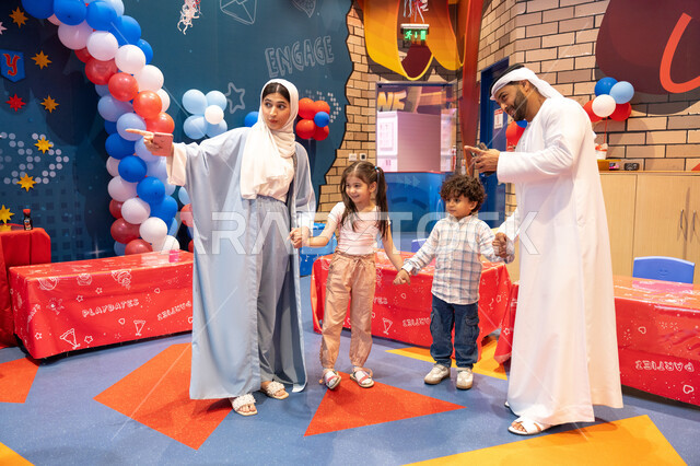 المراكز الترفيهيه المسلية في الامارات العربية،قضاء أوقات سعيده في أرض المرح، عائله عربيه خليجيه اماراتيه تستمتع باللعب فى مدينة الملاهي، ام اماراتيه تشير الى مكان ما ،مفهوم التسلية والترفيه، مشاعر المتعة والفرح،الانشطة الترفيهية الممتعه