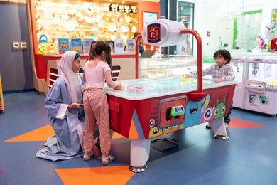 A fun-filled atmosphere, spending happy times with family members, a colorfully illuminated table, fun sports activities, a challenging and exciting competition, entertainment centers in the UAE, an Arab Gulf Emirati family enjoying air hockey in an amusement park.