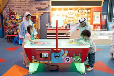 منافسة مليئة بالتحدي والإثارة ، مراكز الالعاب الترفيهيه في الامارات، قضاء اوقات سعيده مع افراد الاسره ،الأنشطة الرياضية الممتعة، طاولة مضيئة بألوان زاهية ، أجواء مليئة بالمرح والسرور، عائله عربية خليجية إماراتية تستمتع بلعب الهوكي الهوائي فى مدينه الالعاب