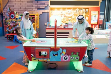 مراكز الالعاب الترفيهيه في الامارات، قضاء اوقات سعيده مع افراد الاسره ،منافسة مليئة بالتحدي والإثارة ، الأنشطة الرياضية الممتعة، طاولة مضيئة بألوان زاهية ، أجواء مليئة بالمرح والسرور، عائله عربية خليجية إماراتية تستمتع بلعب الهوكي الهوائي فى مدينه الالعاب