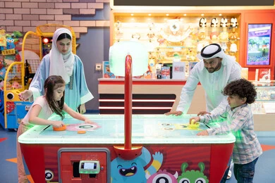 أجواء مليئة بالمرح والسرور،  قضاء اوقات سعيده مع افراد الاسره ،منافسة مليئة بالتحدي والإثارة ، الأنشطة الرياضية الممتعة، مراكز الالعاب الترفيهيه في الامارات، طاولة مضيئة بألوان زاهية ، عائله عربية خليجية إماراتية  تستمتع بلعب الهوكي الهوائي فى مدينه الالعاب