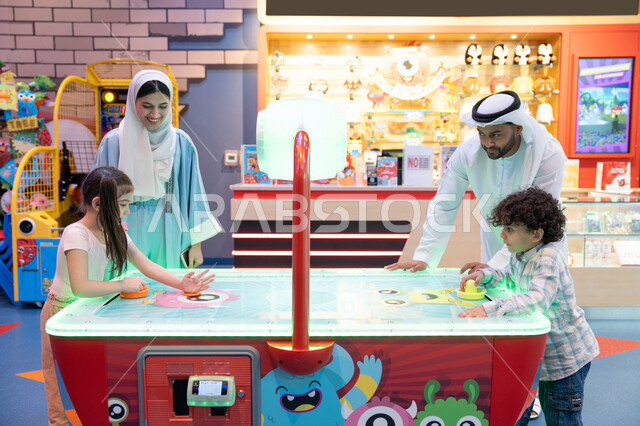 قضاء اوقات سعيده مع افراد الاسره ،منافسة مليئة بالتحدي والإثارة ، الأنشطة الرياضية الممتعة، مراكز الالعاب الترفيهيه في الامارات، طاولة مضيئة بألوان زاهية ،  أجواء مليئة بالمرح والسرور، عائله عربية خليجية إماراتية  تستمتع بلعب الهوكي الهوائي فى مدينه الالعاب